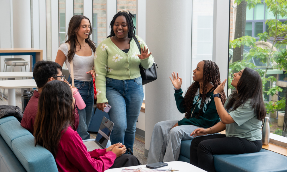 Two students wave as they walk up to a group of seated students