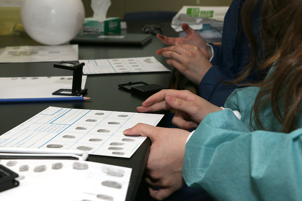 A person's hands seen pressing fingerprints in black ink on to a page